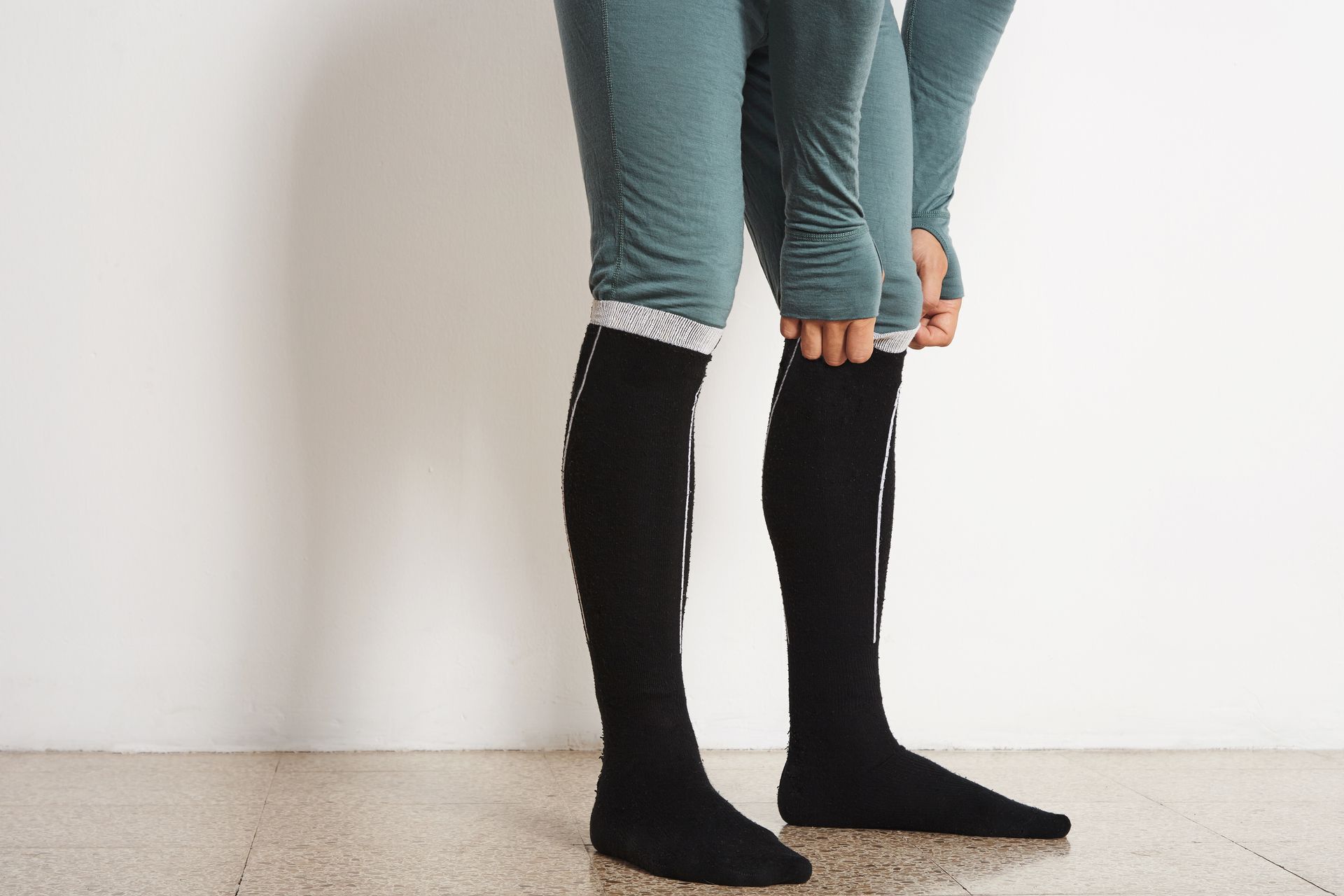 A person is putting on a pair of black knee high socks.