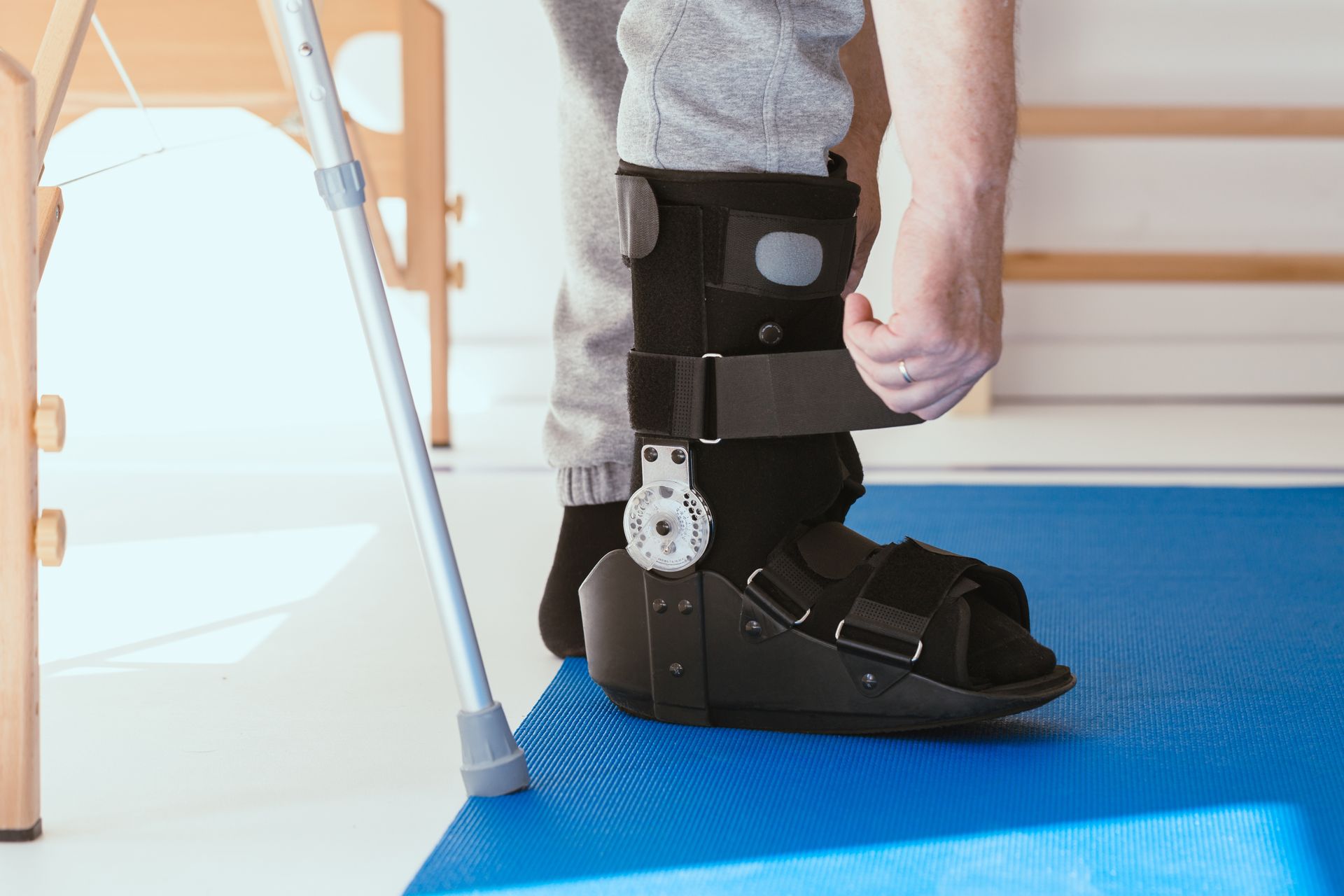 A person is putting on a walker boot on a blue mat.