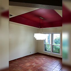 Dining room with red ceiling, white walls, tile floor, chandelier, and window overlooking greenery.