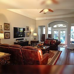 Living room with leather furniture, TV, and art on gray walls. Wooden floors, sunlight.