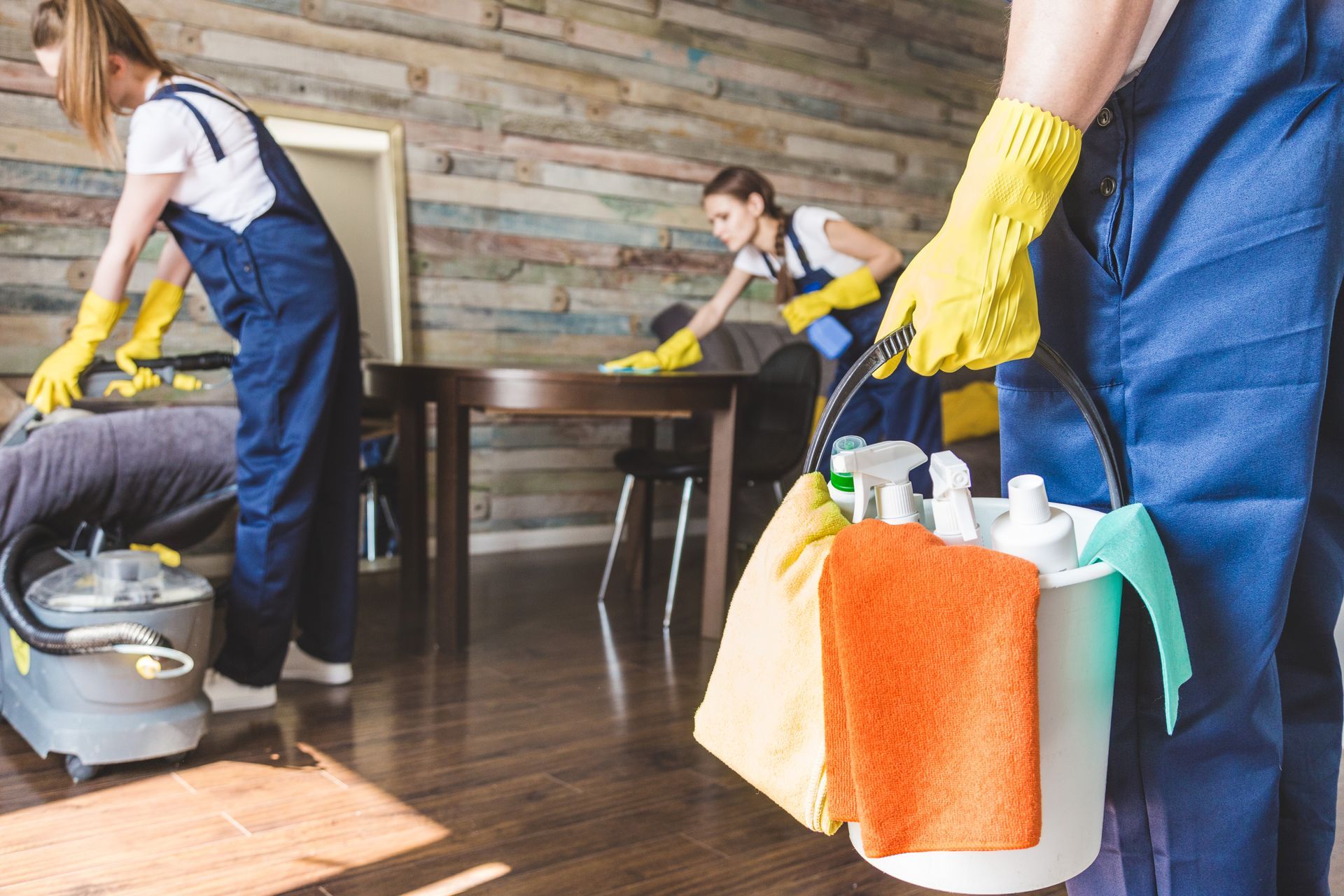 A woman is holding a bucket of cleaning supplies while cleaning a room.