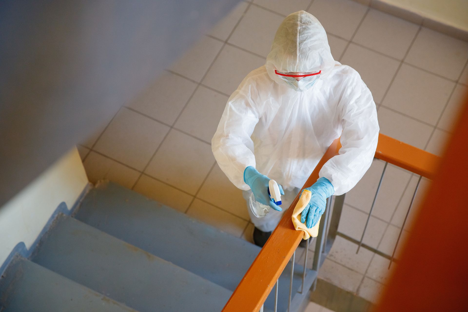 A man in a protective suit is cleaning the railing of a staircase.