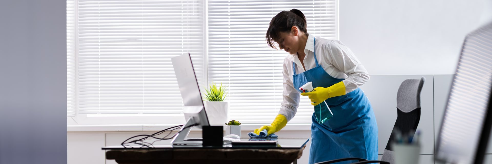 Cleaning a desk with a spray bottle in an office.