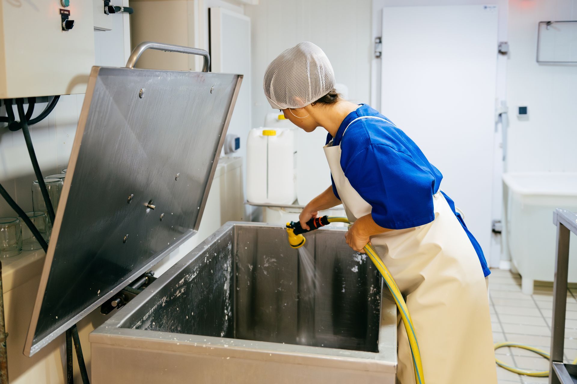 A woman is washing a container with a hose in a kitchen. i
