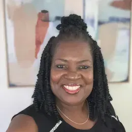 A woman is sitting at a desk with a laptop and a vase of flowers.