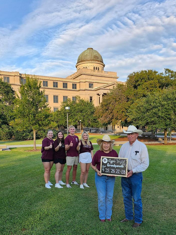 A group of people are standing in a grassy field in front of a large building.