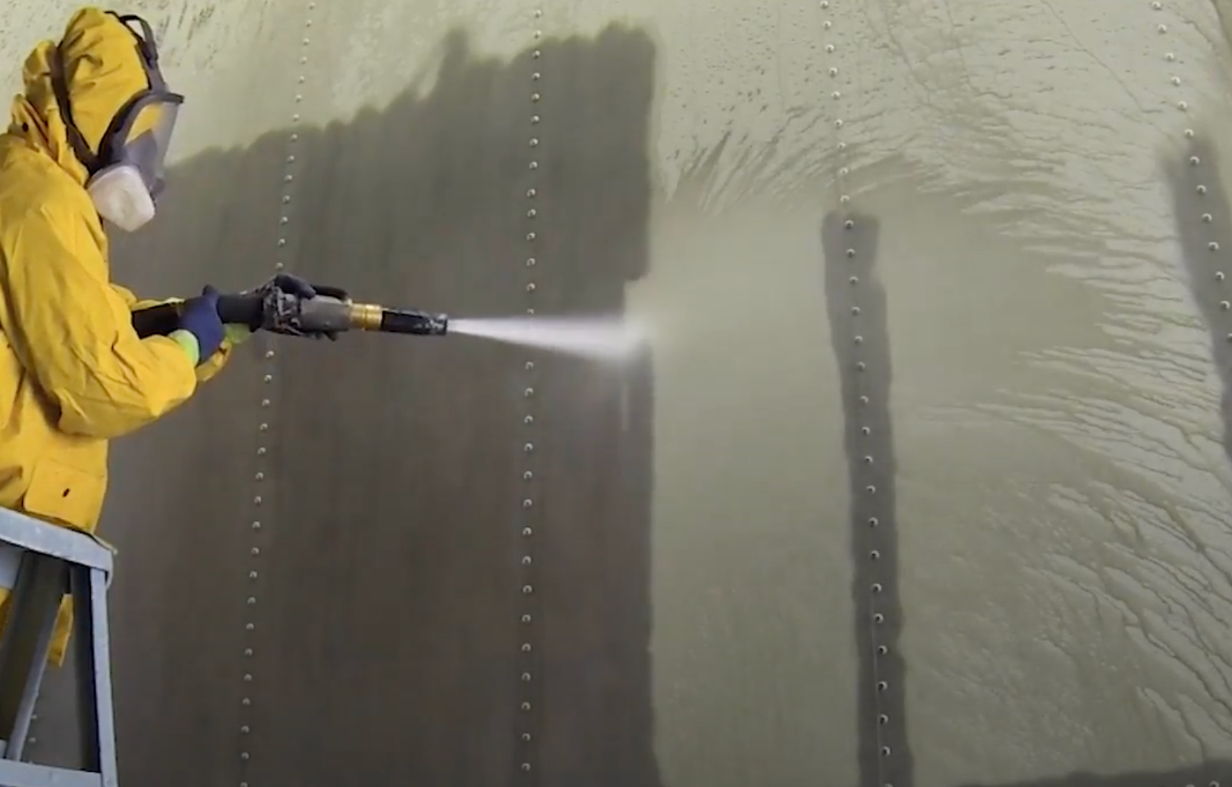 A man in a yellow jacket is spraying something on a wall.