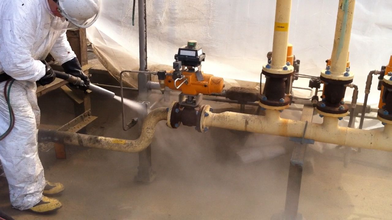 A man in a protective suit is cleaning pipes with a high pressure washer.