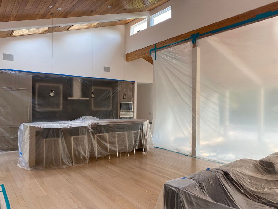 A living room with a kitchen and sliding glass doors covered in plastic.