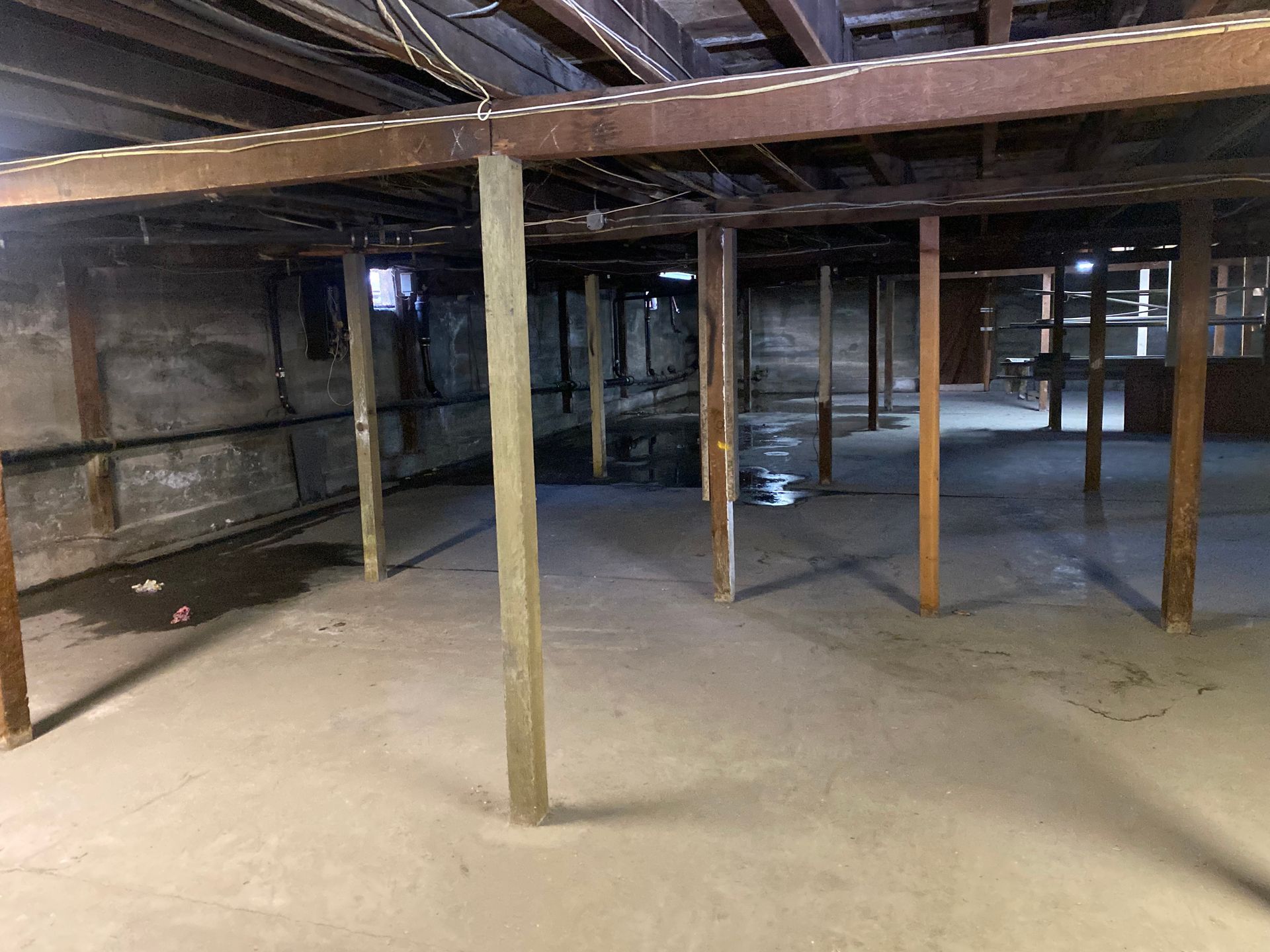 An empty basement with wooden beams and a concrete floor.