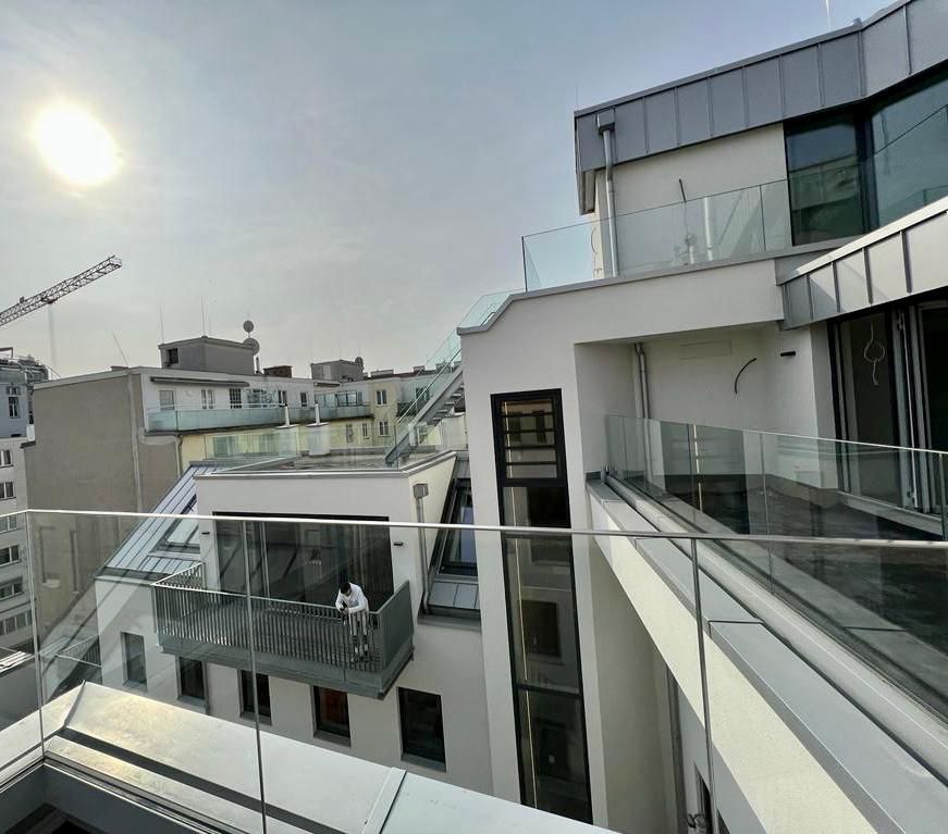 Außenansicht moderner Gebäude mit Glasbalkonen an einem sonnigen Tag. Eine Person steht auf einem der Balkone.