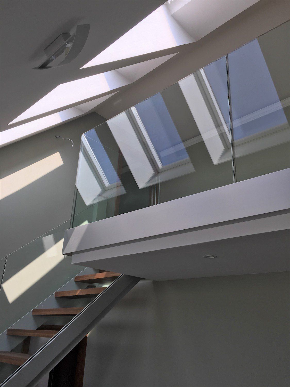 Modernes Interieur: Treppe mit Holzstufen, Glasgeländer und Oberlichtern, die Schatten werfen.