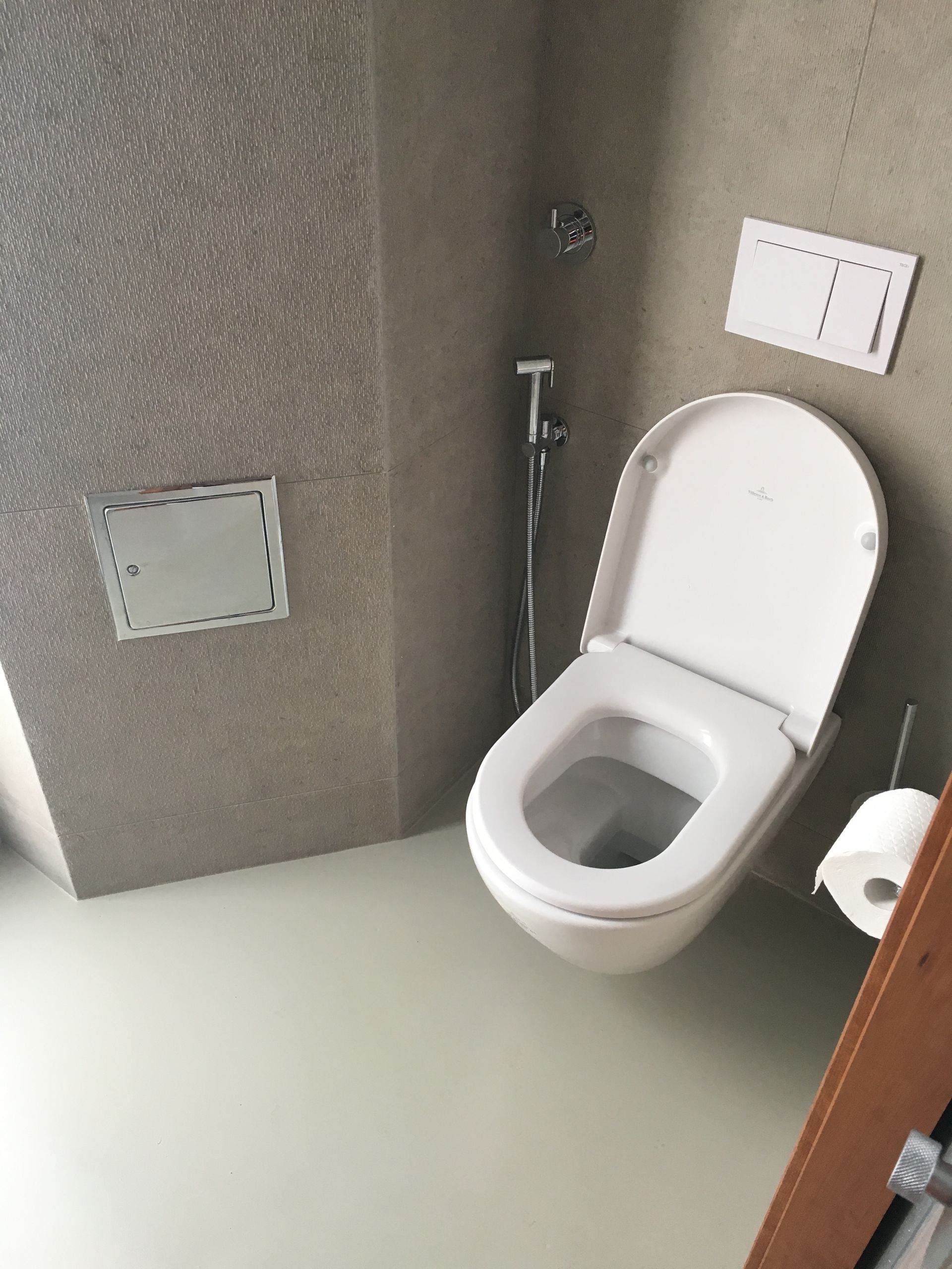 Toilette in einem modernen Badezimmer mit hellgrauen Wänden, weißer Toilette und einer Rolle Toilettenpapier.