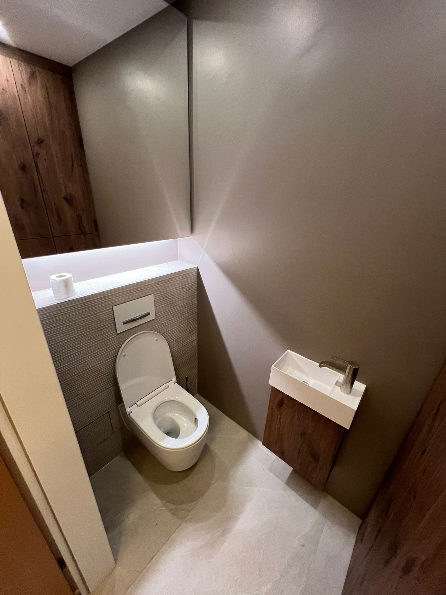 Kleines, modernes Badezimmer mit Toilette, Waschbecken und Holzvertäfelung.