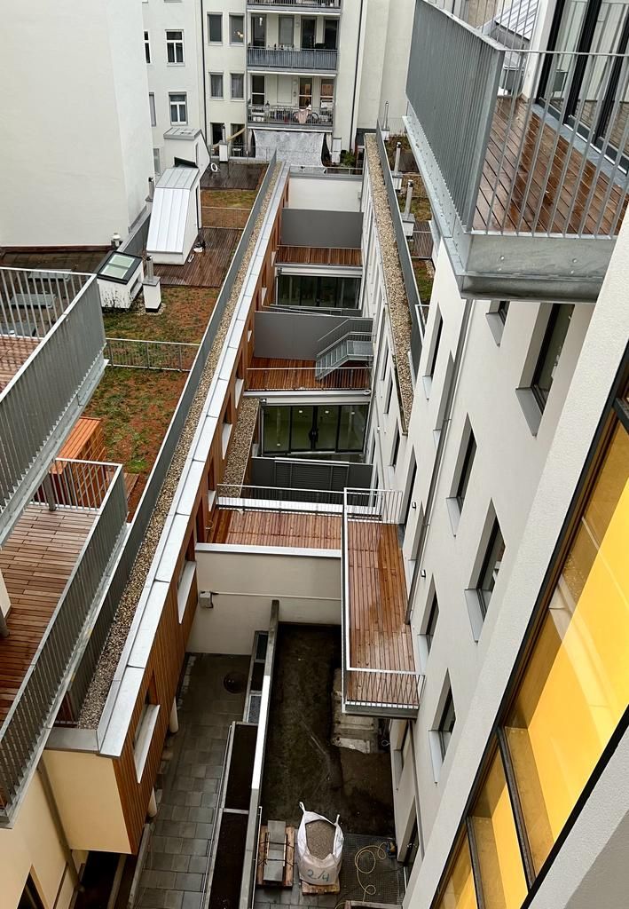 Draufsicht auf einen schmalen Innenhof zwischen Gebäuden; einige mit Gründächern, andere mit Fenstern und Balkonen.