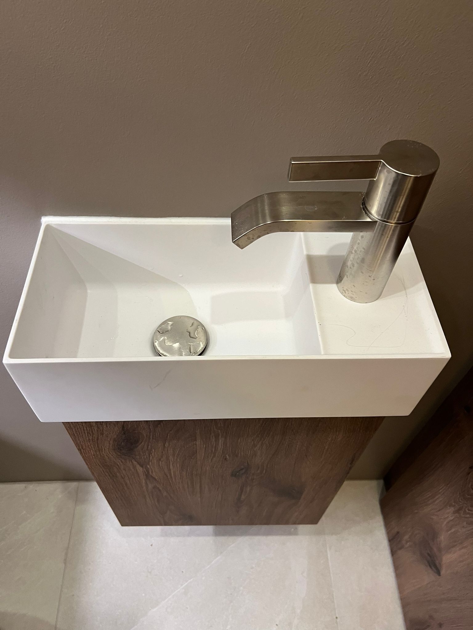 Weißes, rechteckiges Waschbecken mit gebürsteter Silberarmatur, auf einem dunklen Holzsockel.