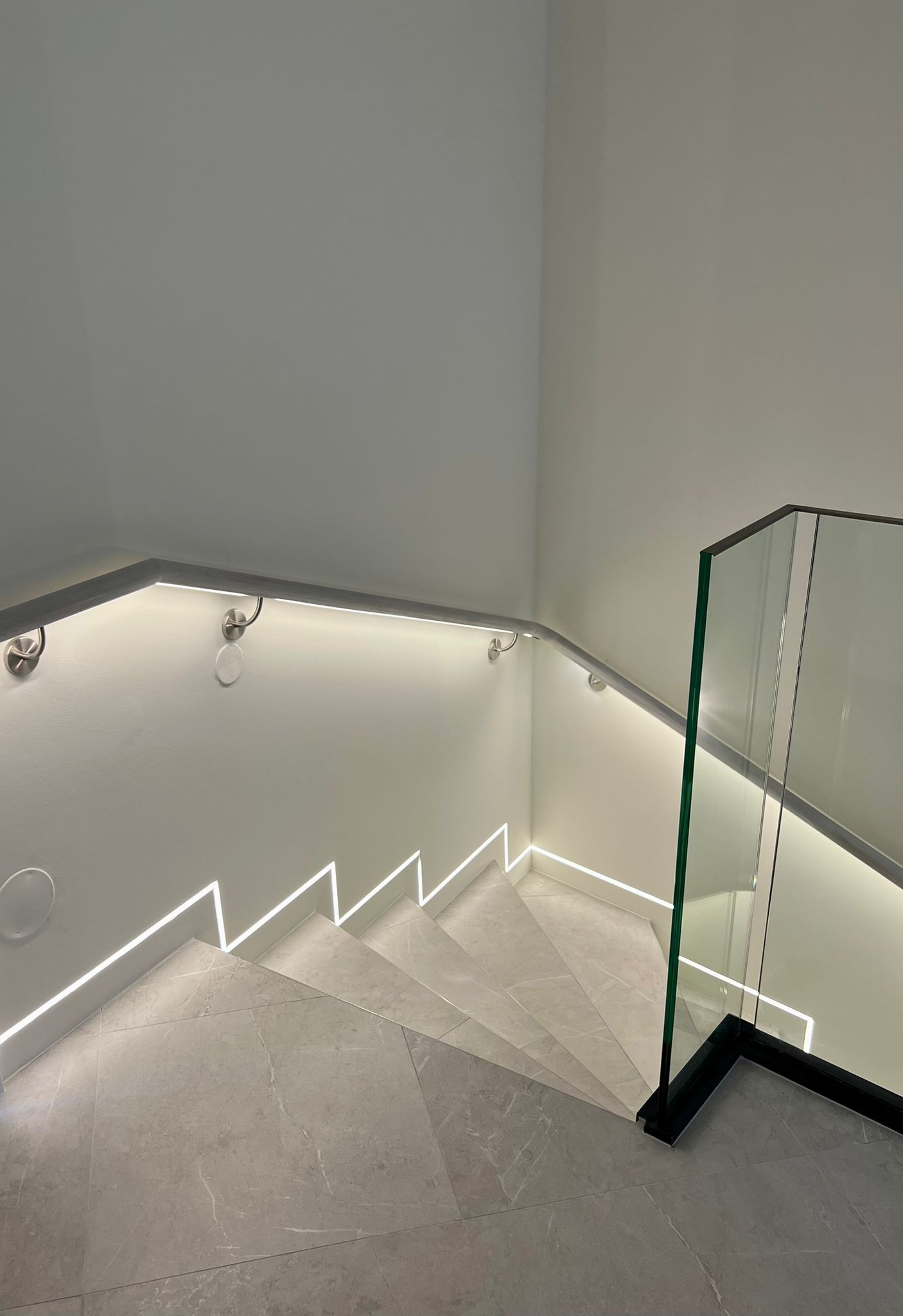 Treppenhaus mit integrierter LED-Beleuchtung. Glasgeländer auf einer Seite. Weiße Wände und Treppe.