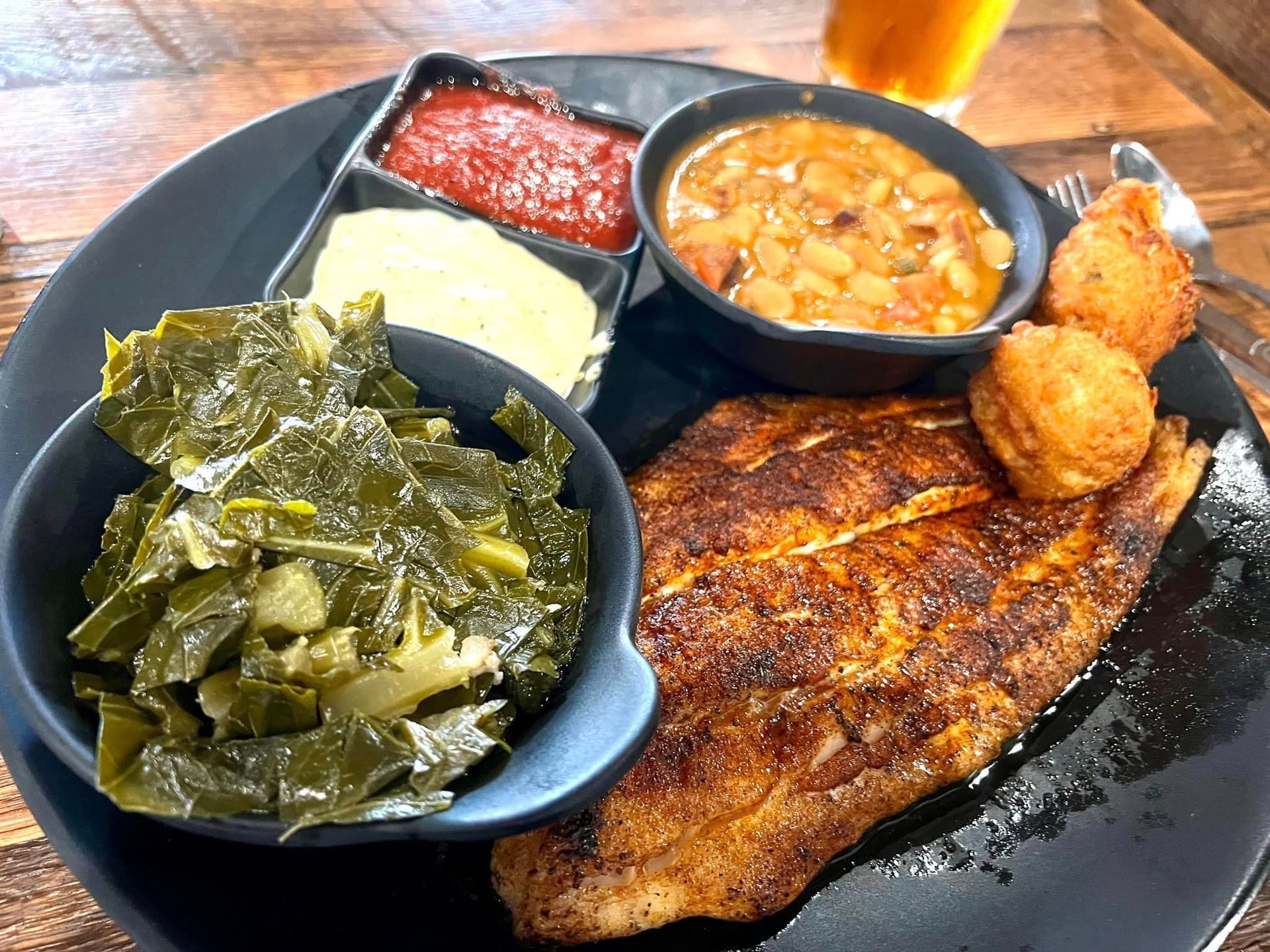 A plate of food with meat , beans , and collard greens on a table.