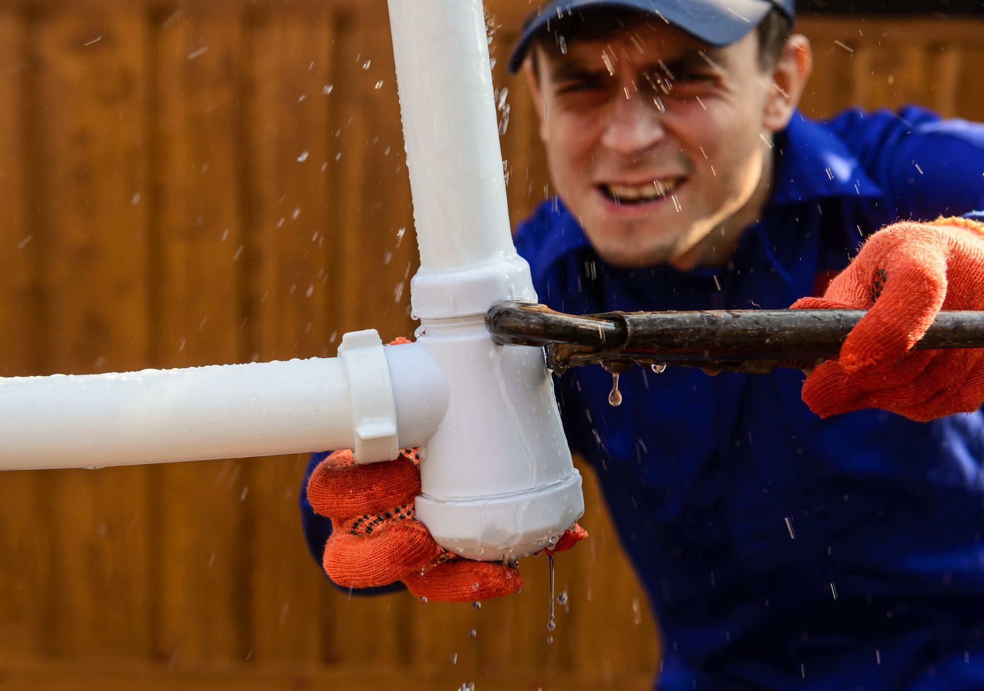 Plumber in blue overalls repairing leaking pipe with wrench. Plumber in blue overalls repairing leaking pipe with wrench.