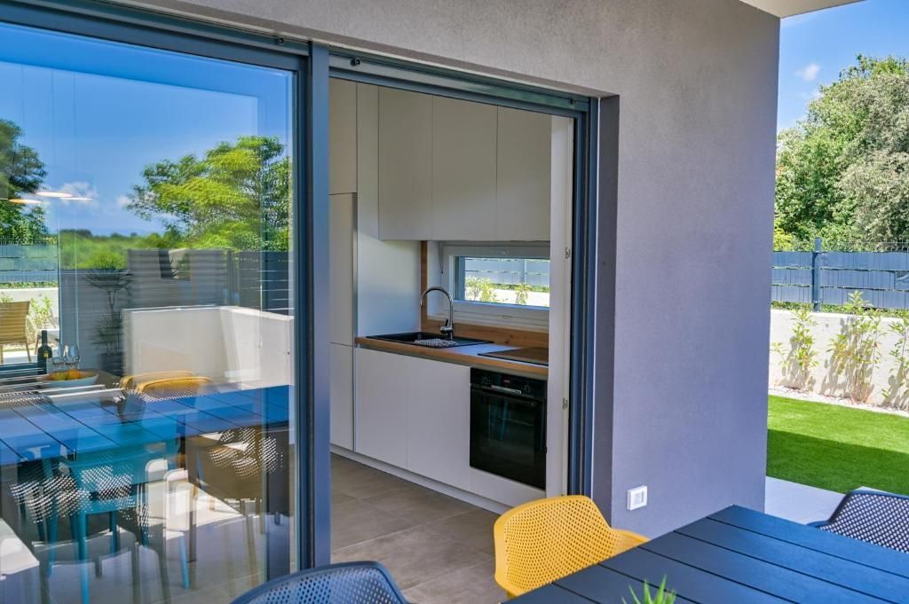 Terasa z mizo in stoli ter kuhinja z drsnimi steklenimi vrati.