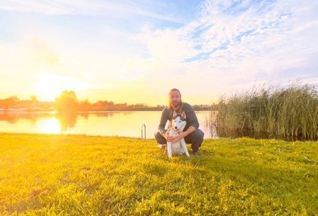 Healingen met dieren. Een man knielt neer naast een hond in een veld.