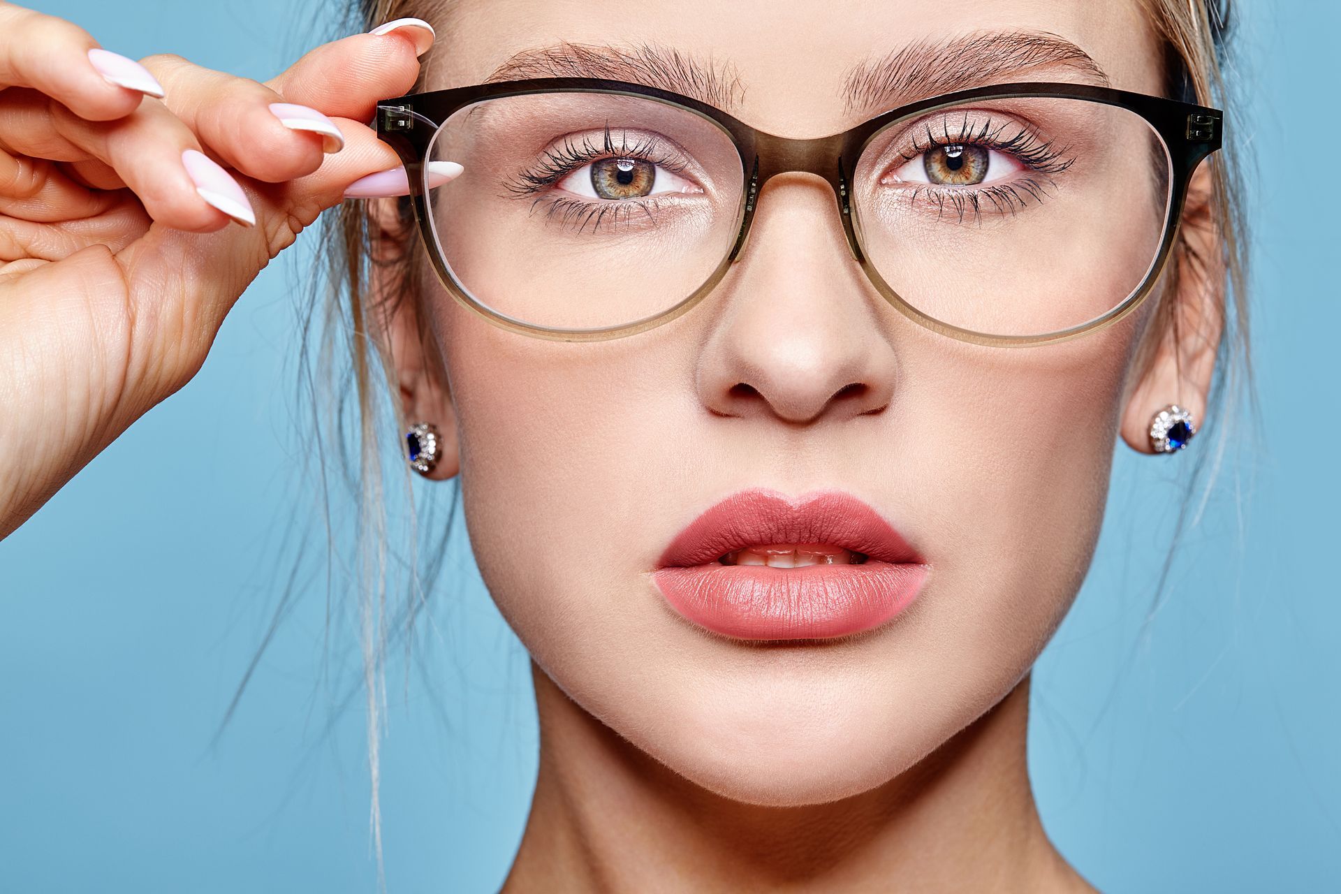 Woman with wavy hair wearing black-rimmed glasses and dark lipstick, looking up.