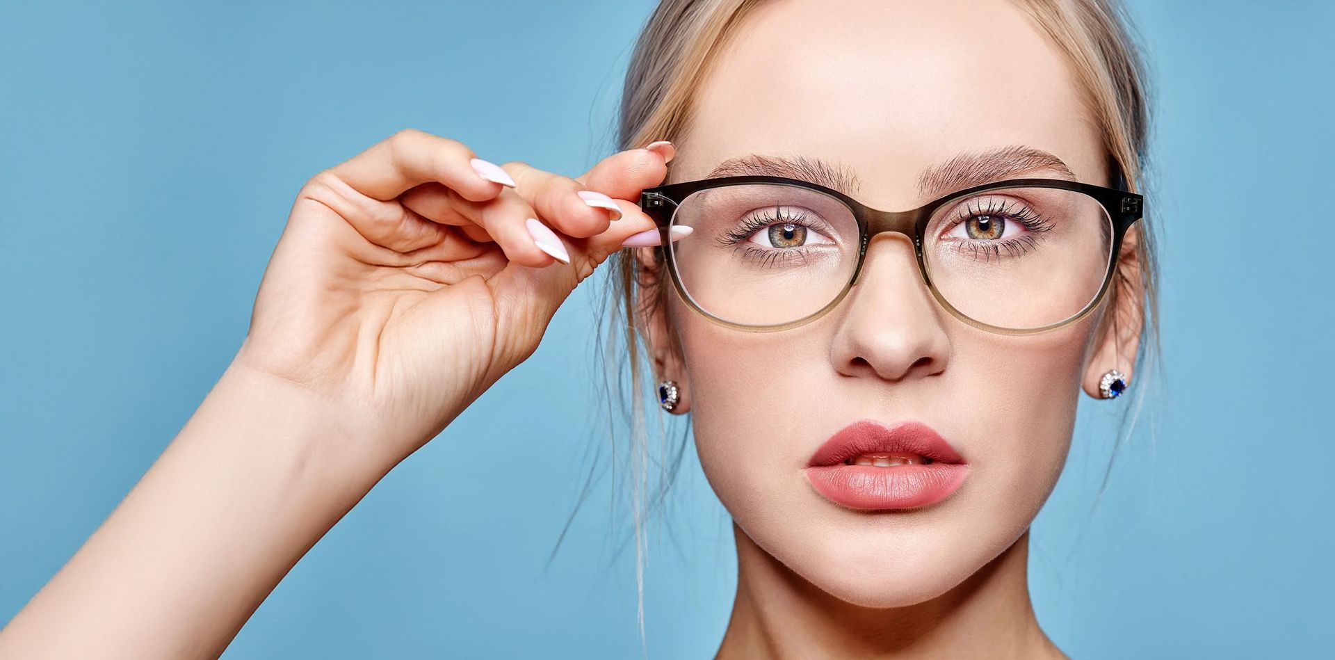 Woman with wavy hair wearing black-rimmed glasses and dark lipstick, looking up.