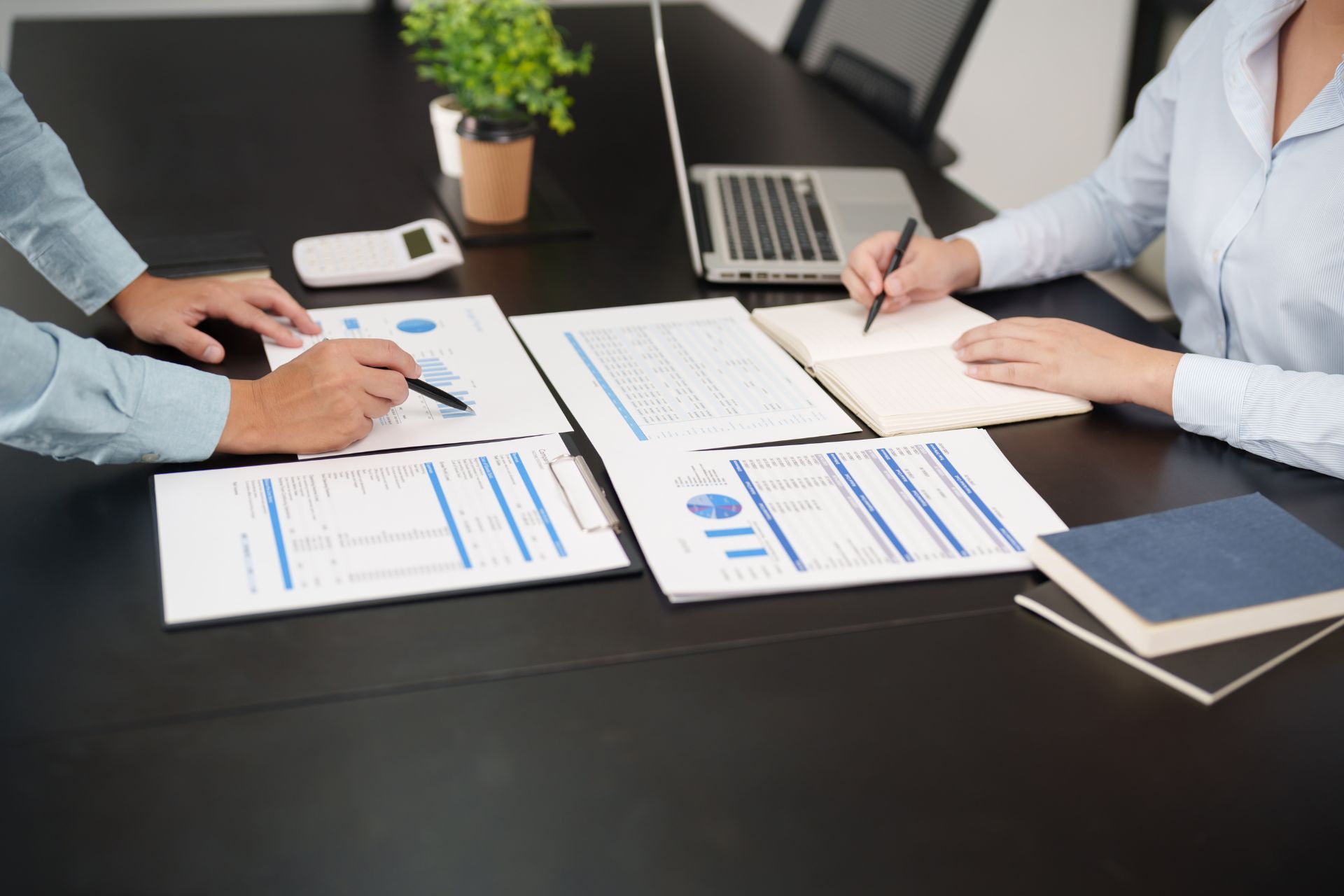 a man and a woman are sitting at a table with papers and a laptop .