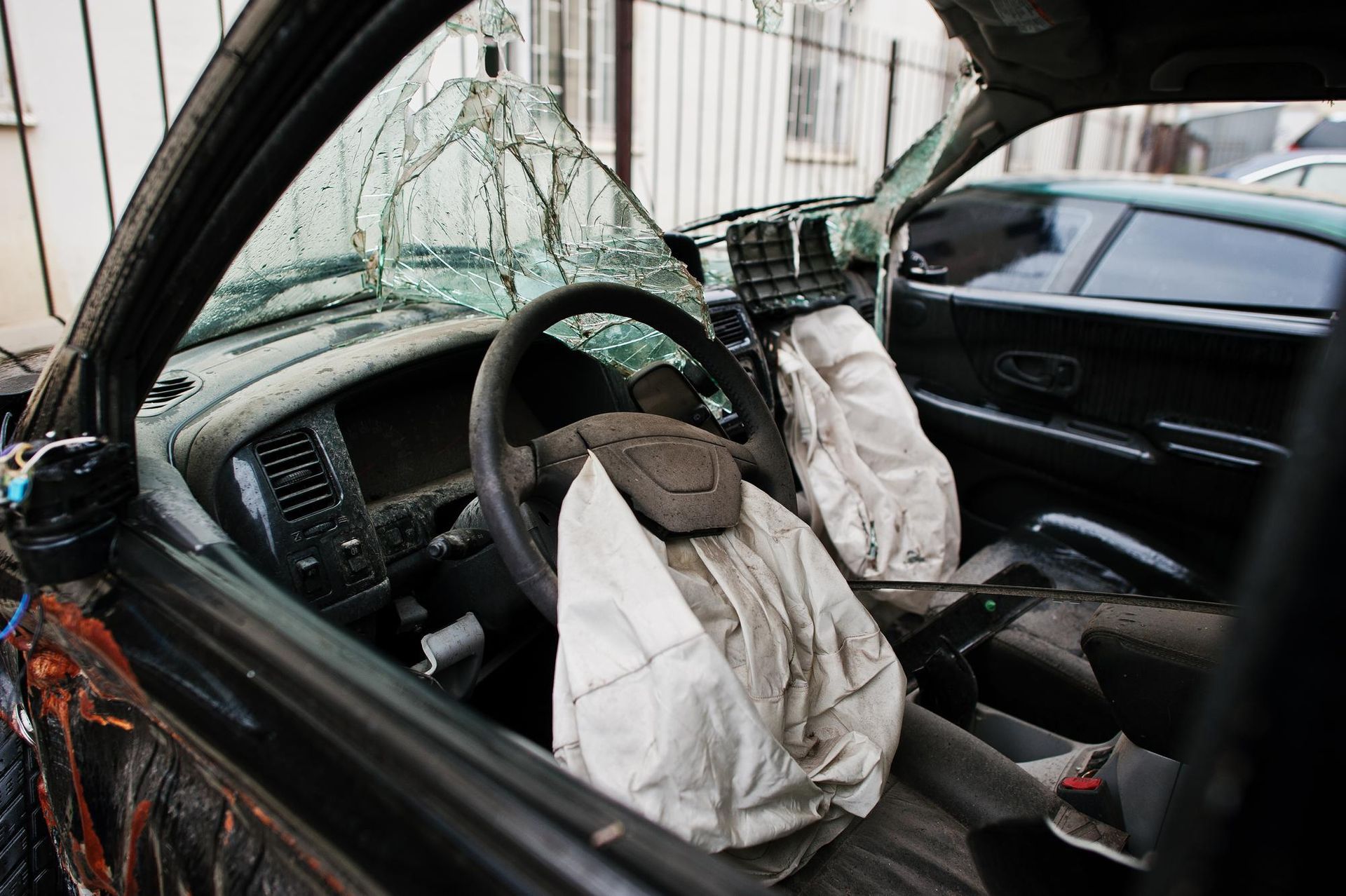 Interior view of a damaged vehicle with deployed airbags and a shattered windshield.
