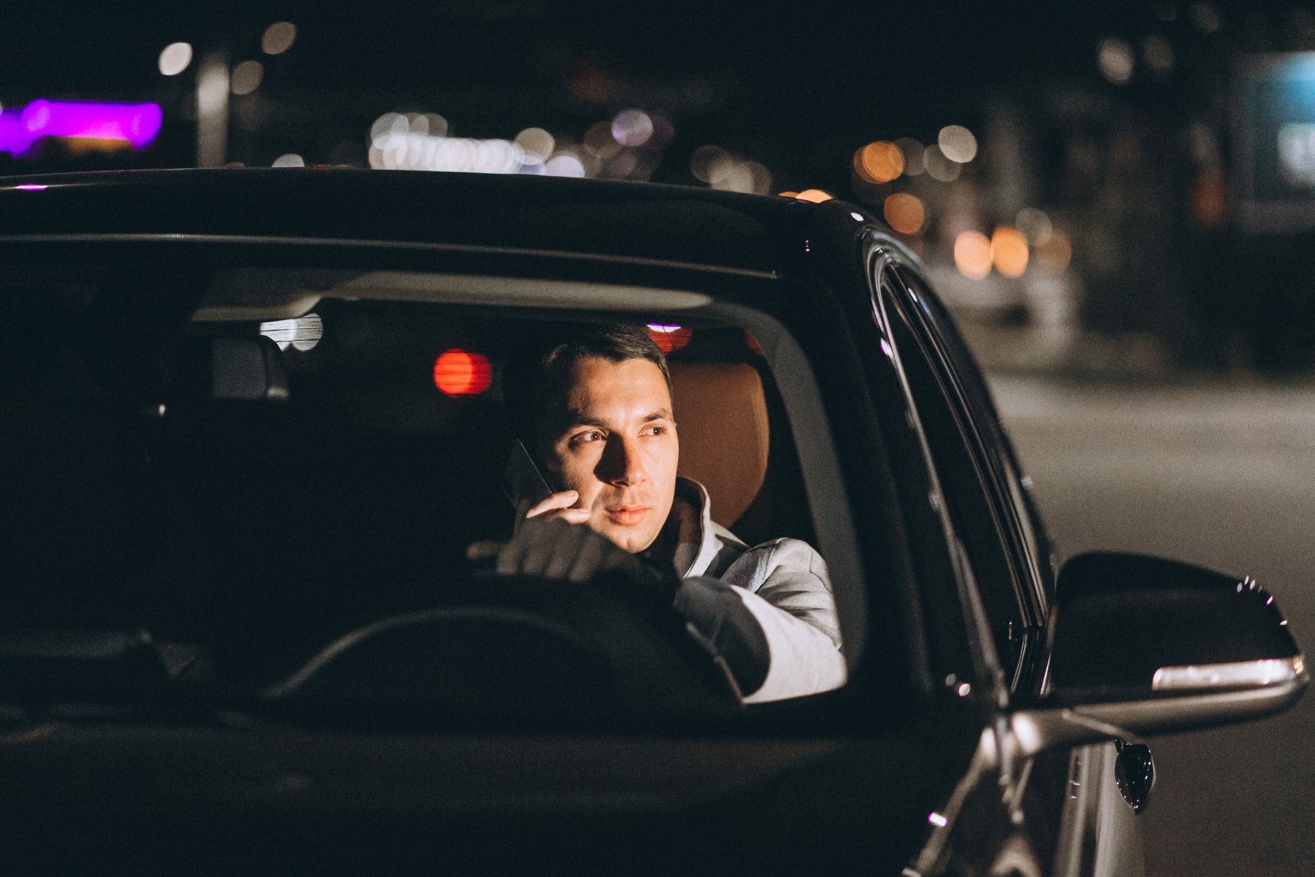 A person driving a car at night, holding a phone to their ear while looking ahead.