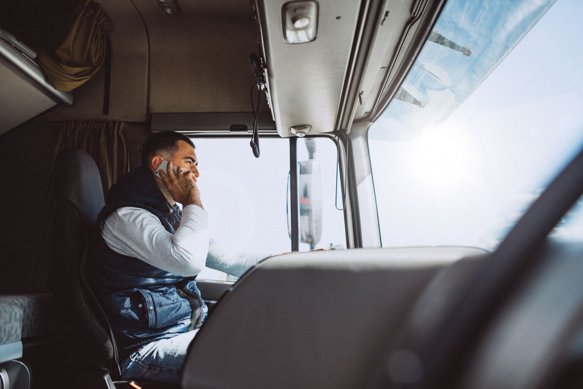 A person sits in the driver’s seat of a truck, looking out the window while holding a smartphone to their ear.
