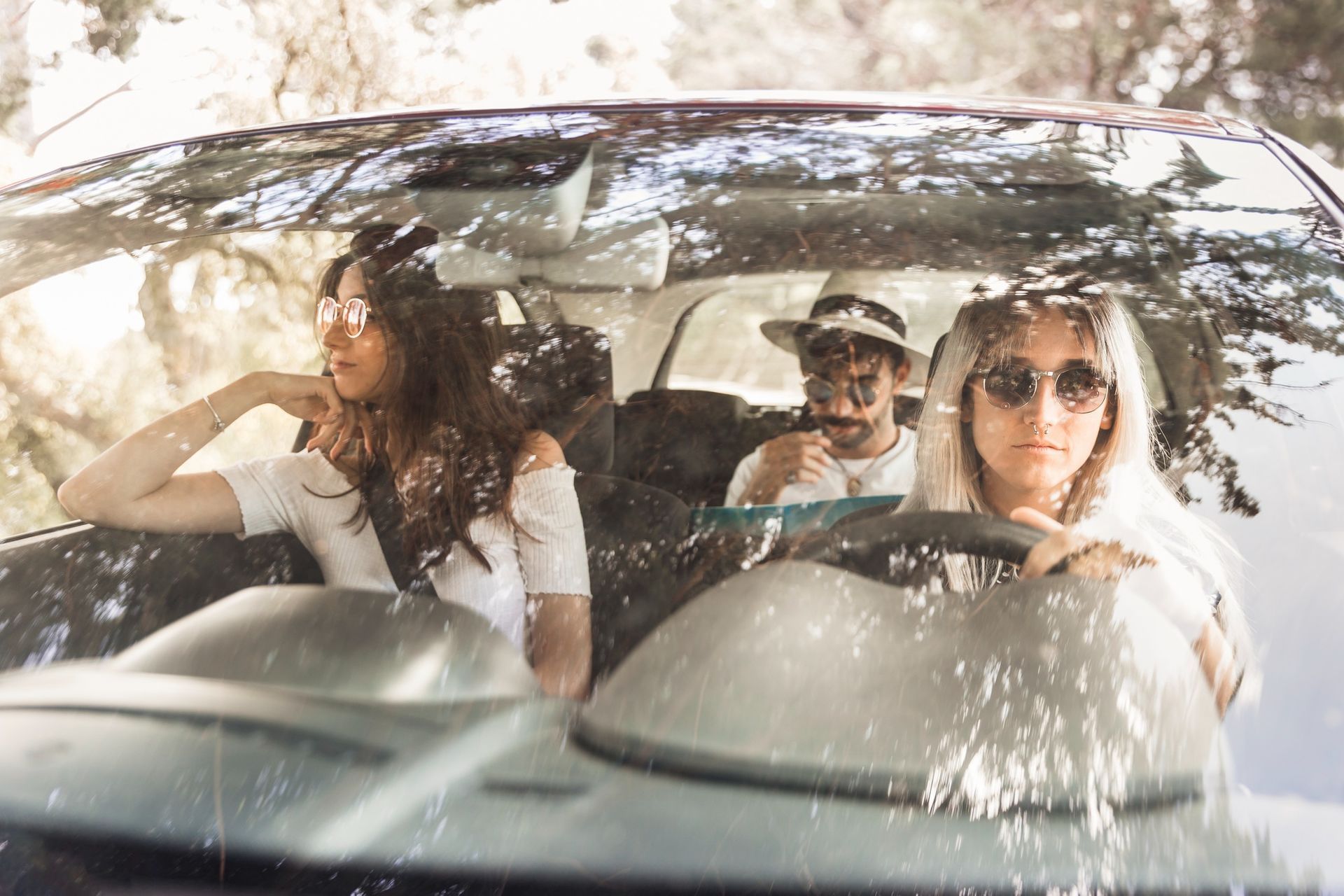 Three people sitting in a car, with one person driving, during a sunny day trip outdoors.