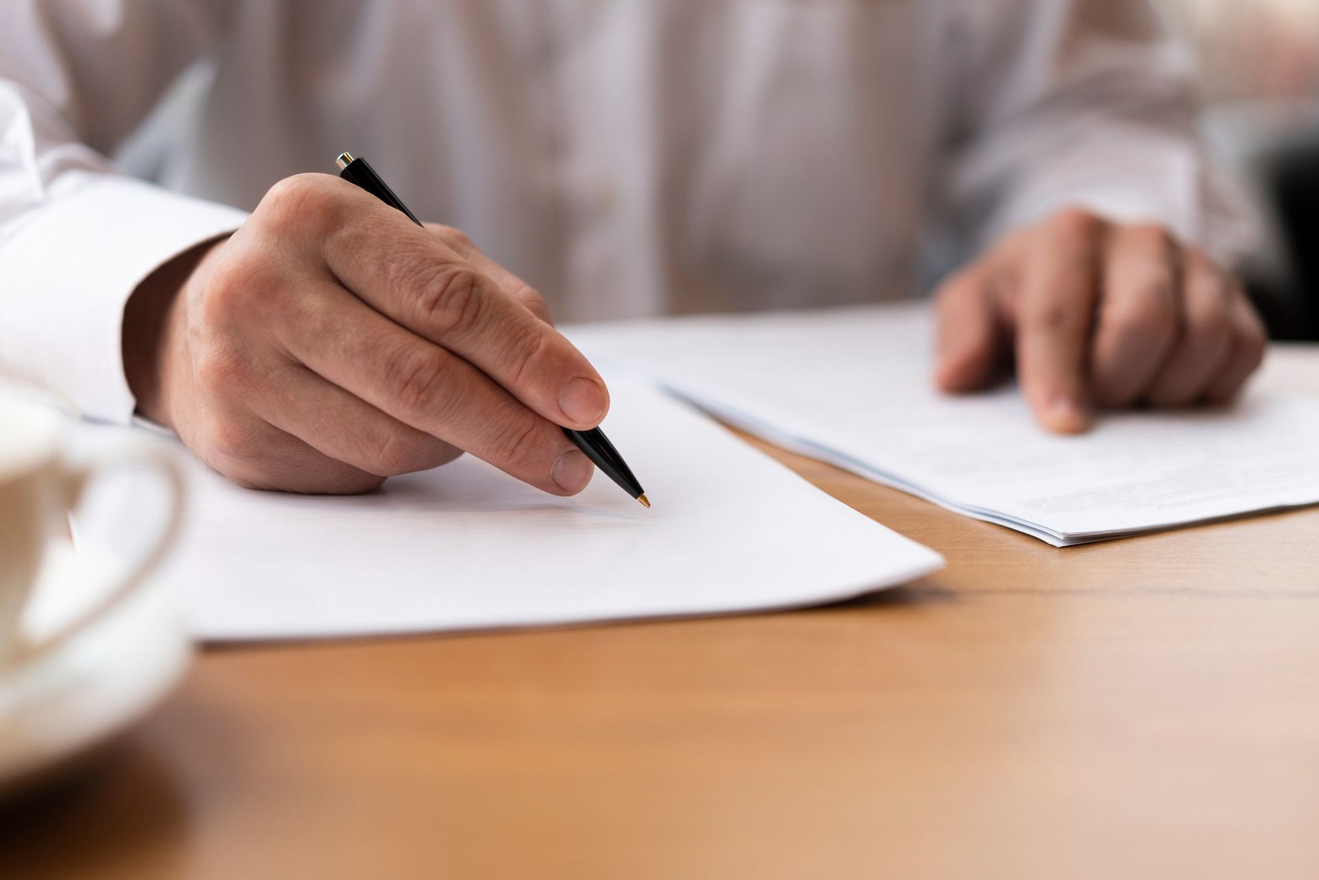 Two people shaking hands over a contract on a desk.