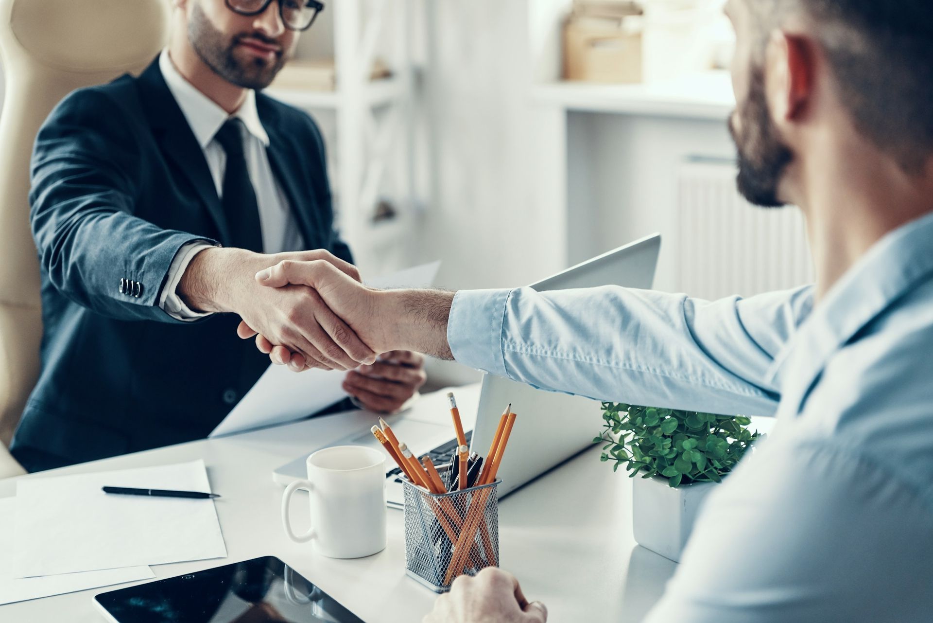 Two people shaking hands over a contract on a desk.