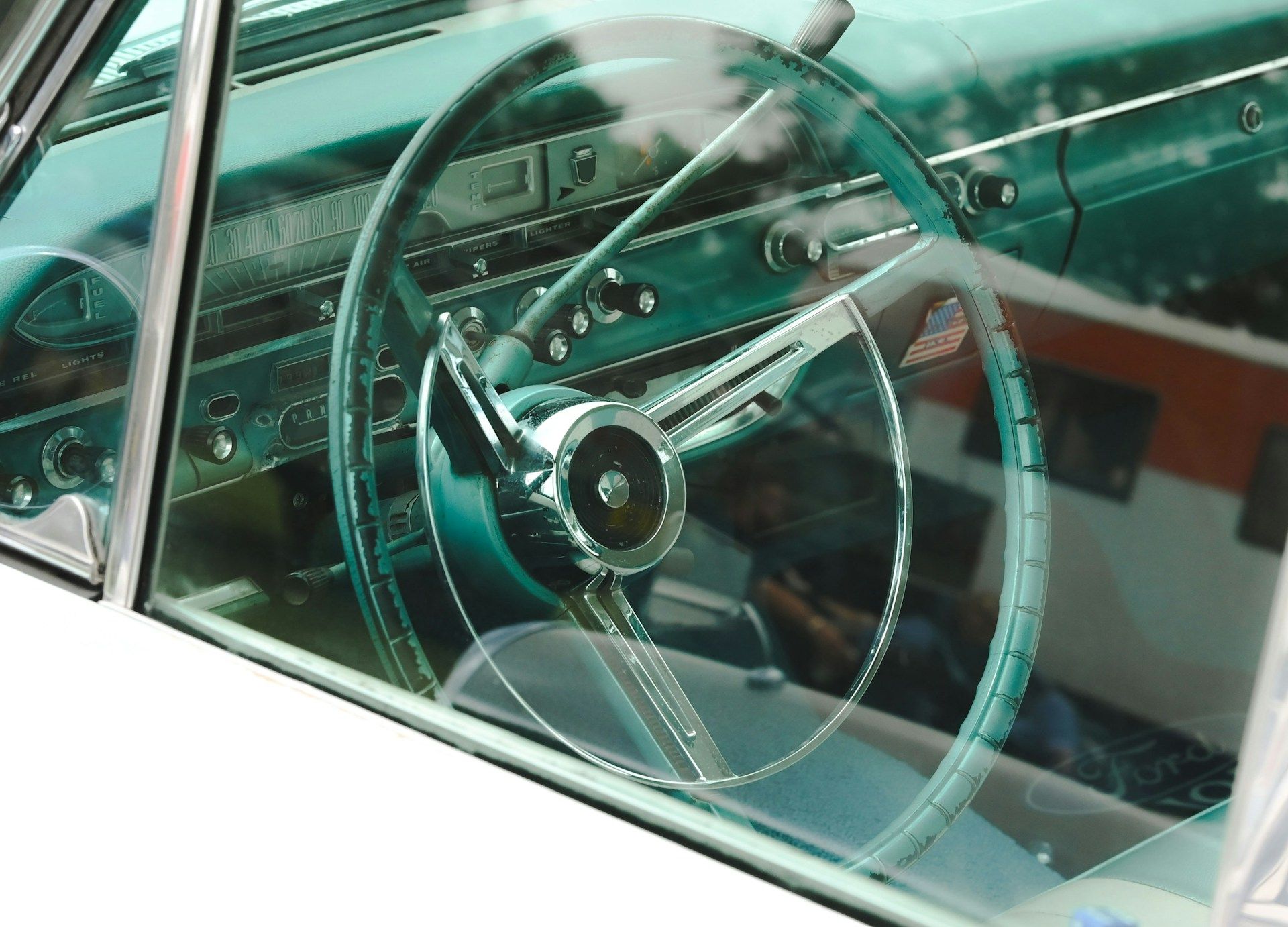 A view through the window of a vintage car, showing a teal dashboard and a large, chrome-trimmed steering wheel.