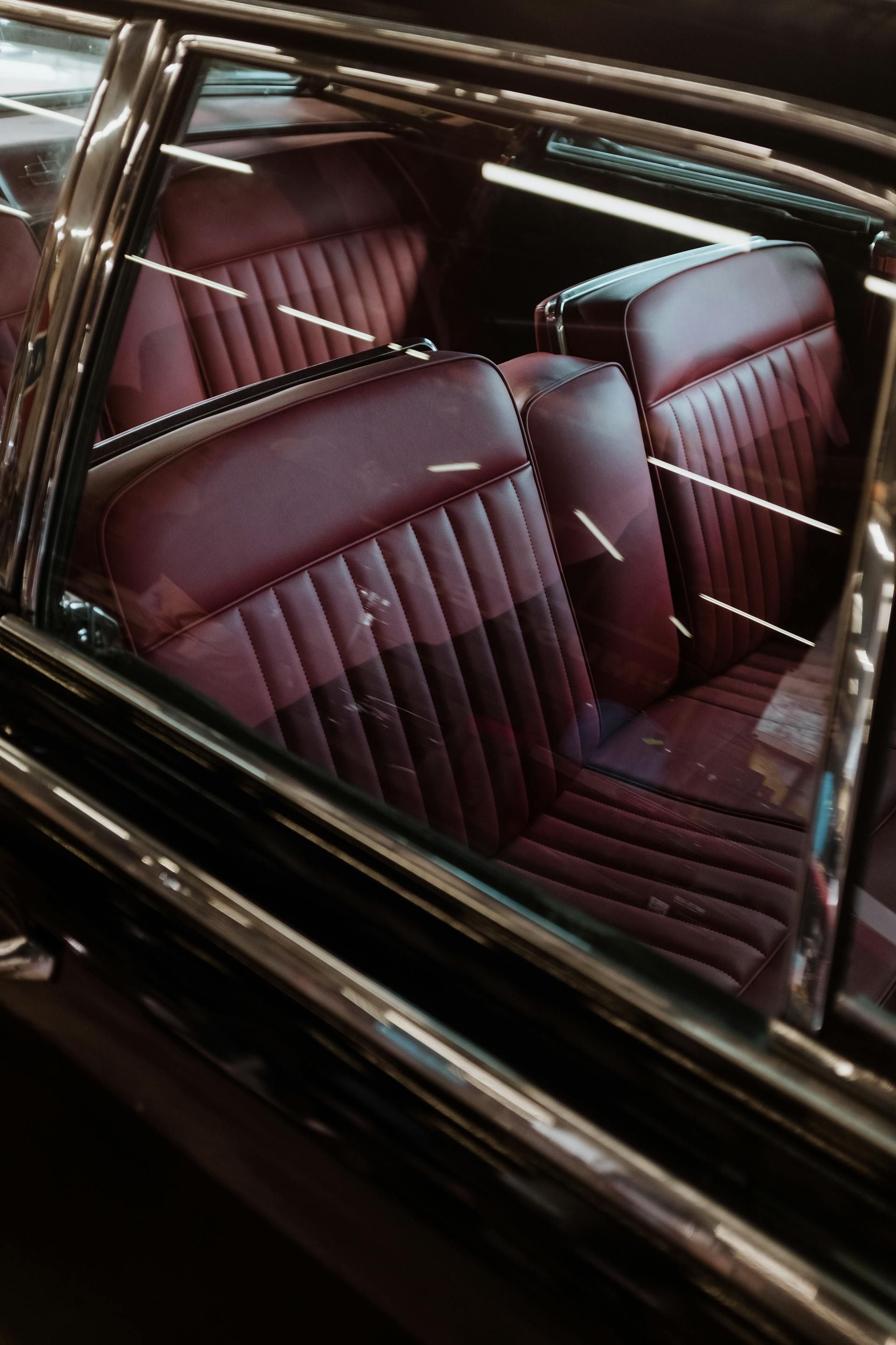 A view through the window of a vintage car showcasing dark red, pleated leather seats.
