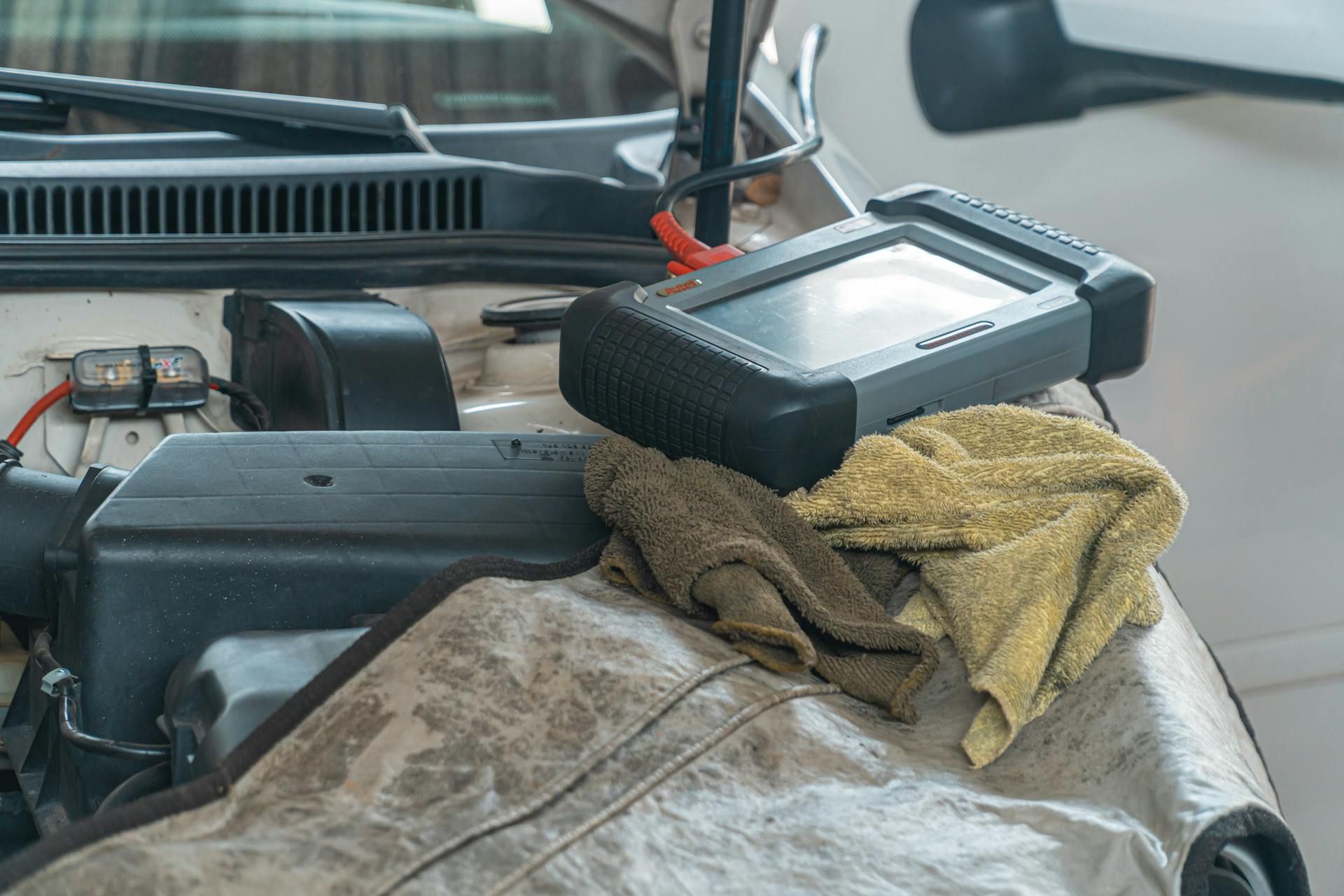 A diagnostic scanner resting on a cloth-covered engine bay while a vehicle is being serviced.