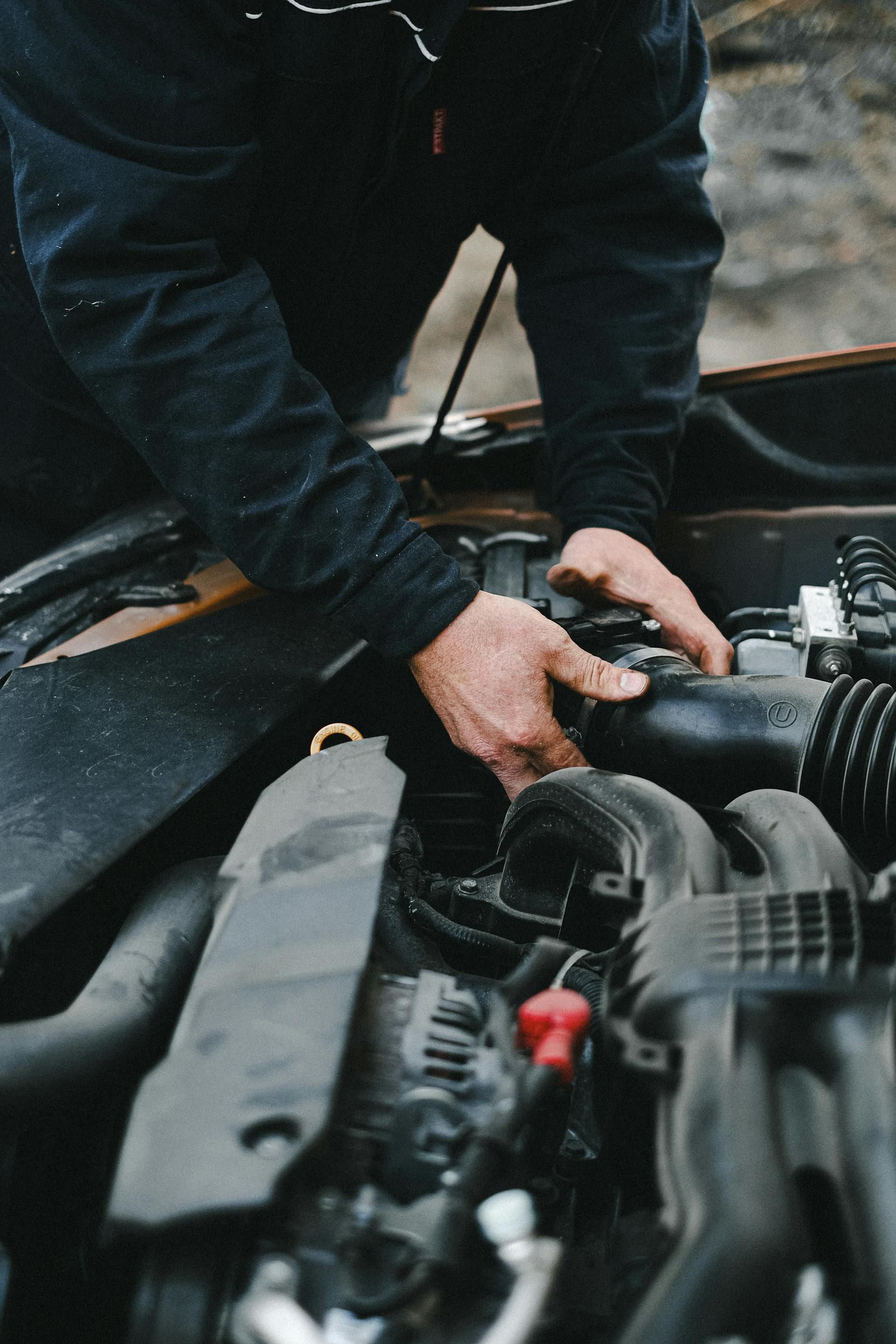 A person wearing a dark jacket performs maintenance on the engine of a vehicle.