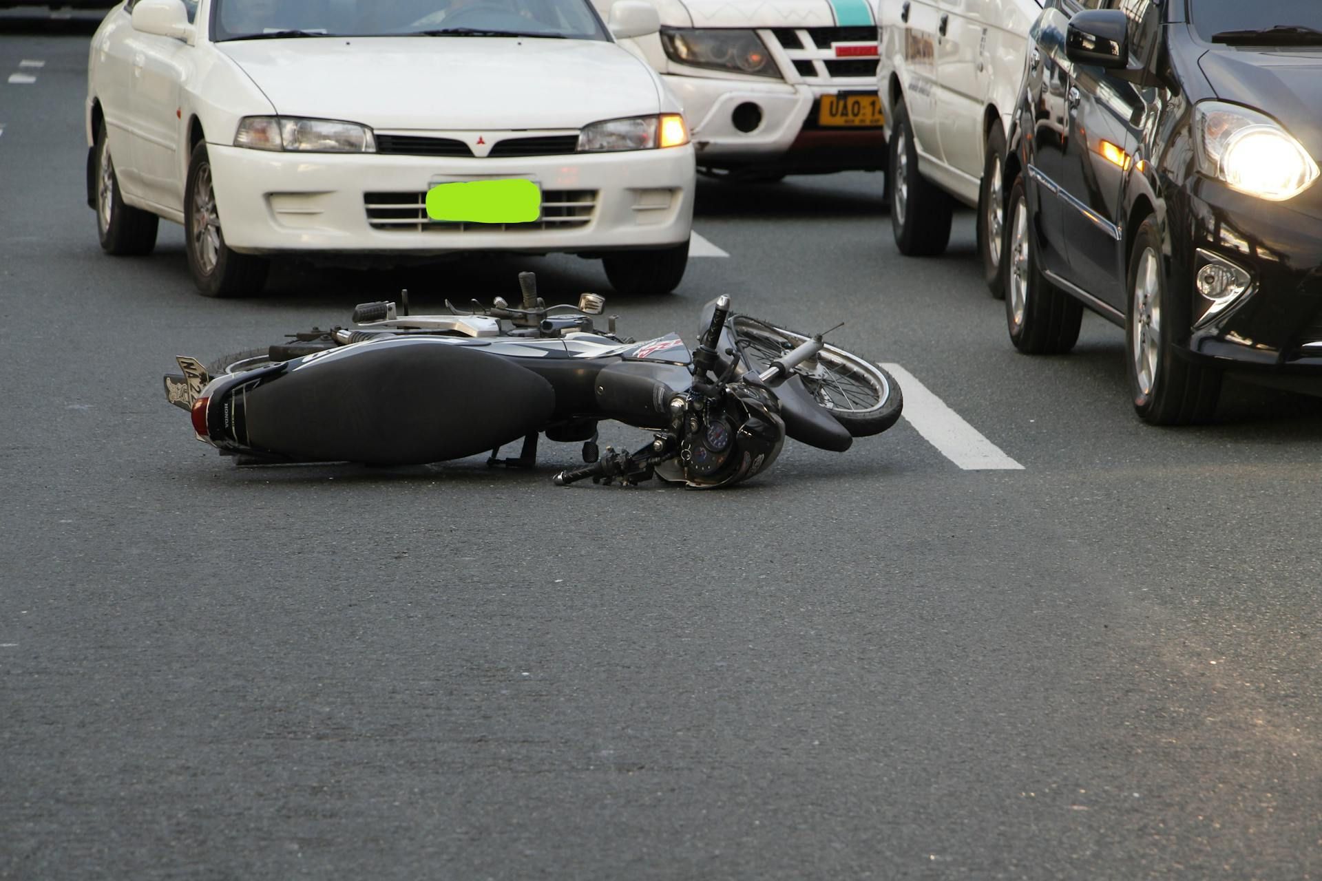 A motorcycle lies on its side in the middle of a city street surrounded by cars.