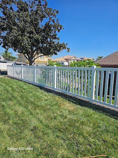 A white fence surrounds a lush green yard with a tree in the background.