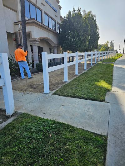 A man is standing next to a white fence in front of a building.
