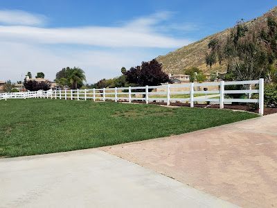 A white fence surrounds a lush green field.