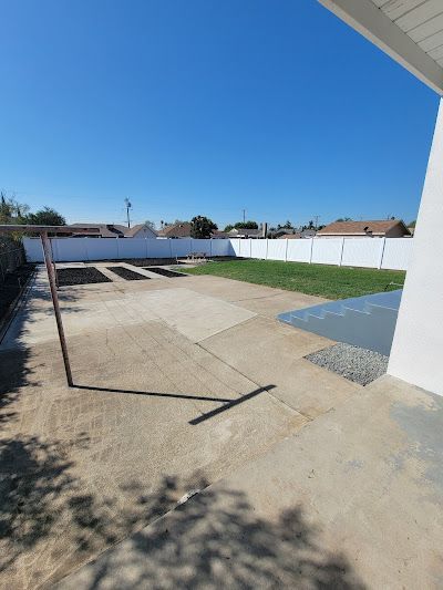 A backyard with a white fence and a concrete patio.
