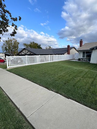 A white fence surrounds a lush green yard in front of a house.