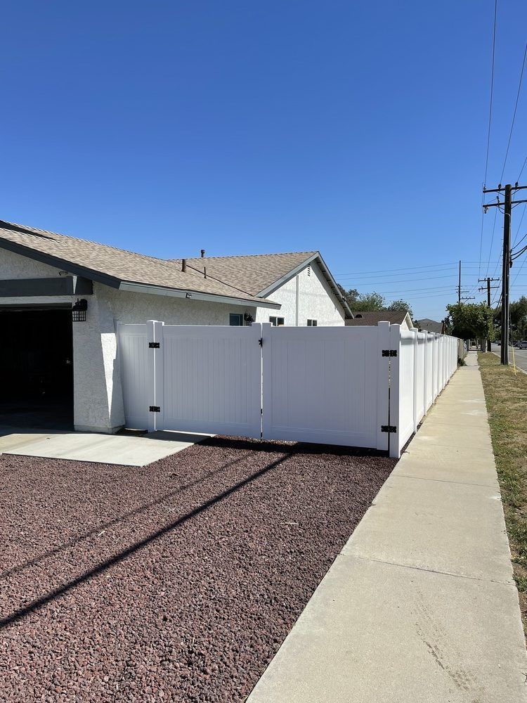 A white fence surrounds a house next to a sidewalk.