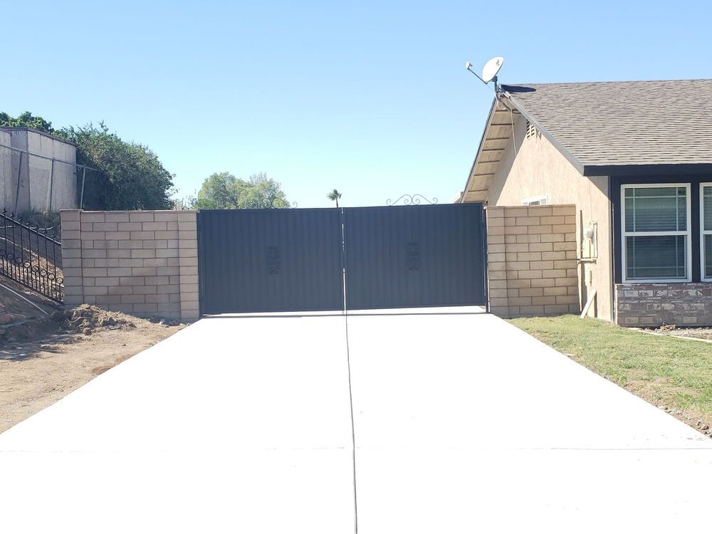 A concrete driveway leading to a house with a black gate