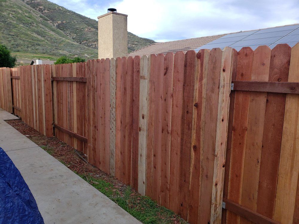 A wooden fence along a sidewalk next to a house with mountains in the background.