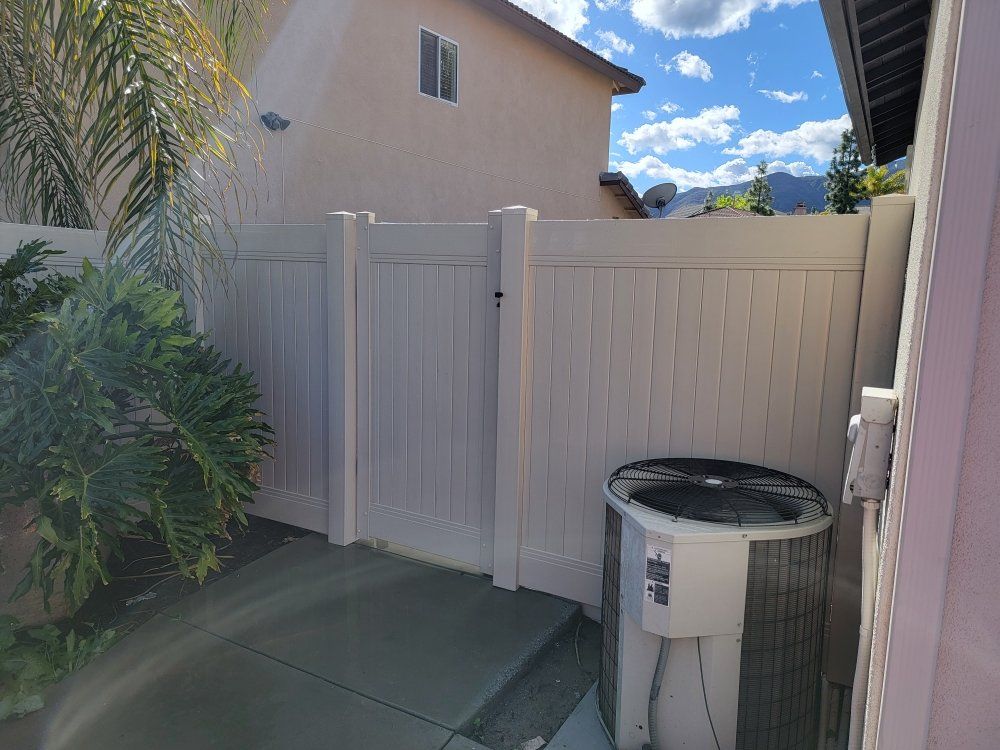 A white fence with a air conditioner in the backyard of a house.