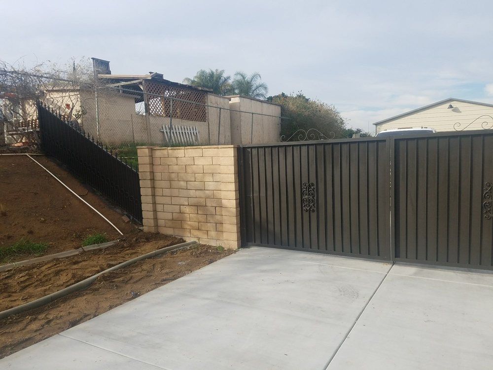 A black gate is surrounded by a brick wall and a concrete driveway.