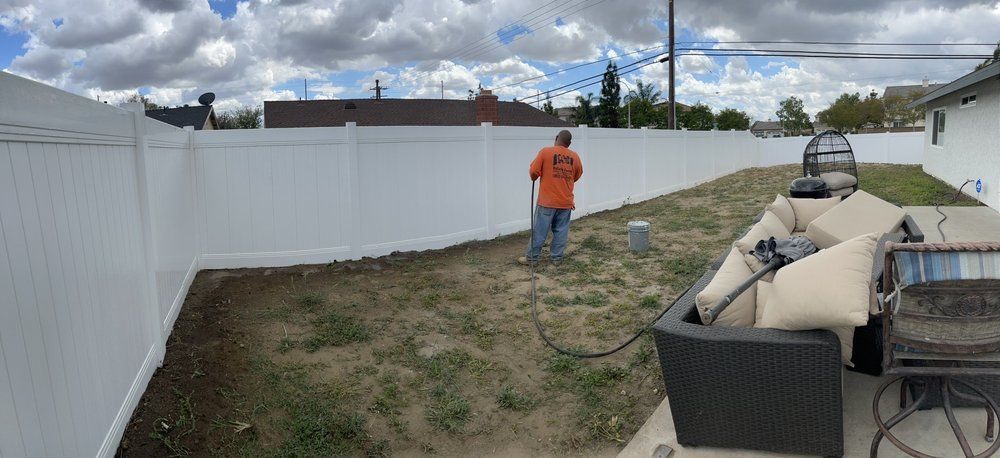 A man is standing in a backyard next to a white fence.